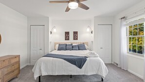 A bedroom with a bed, a ceiling fan, two wall-mounted lights, a window with curtains, and a wooden dresser.