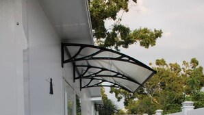 Un estrecho pasillo exterior con suelo de losas de piedra, una valla blanca y un corredor cubierto.
