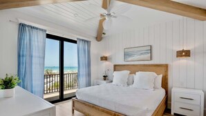 Een slaapkamer met een groot bed, een plafondventilator, een nachtkastje en uitzicht op de oceaan vanaf een balkon.