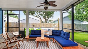 Un patio couvert comprenant un canapé bleu, des chaises en bois et une table basse en bois.