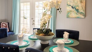 Mesa de jantar com um arranjo central de orquídeas brancas, jogos americanos verde-turquesa e copos de vidro transparente.
