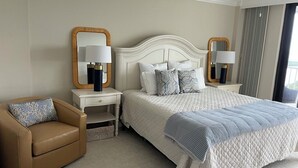 A hotel room with a large bed, two bedside tables with lamps, a chair, and a large mirror on the wall. - Gorgeous 17th fl sunsets @ South Seas 2BR/2BA NEW mattresses updated furnishings (Marco Island)