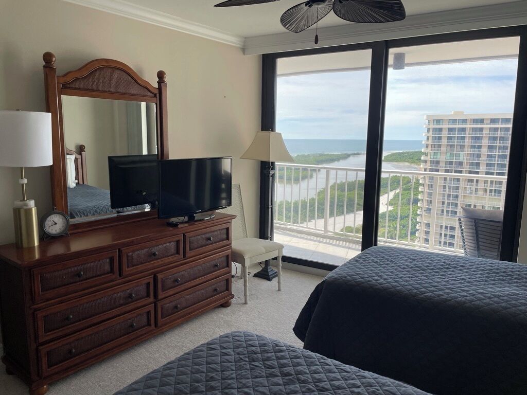 A hotel room with a large window, a wooden dresser, a television, and two beds.