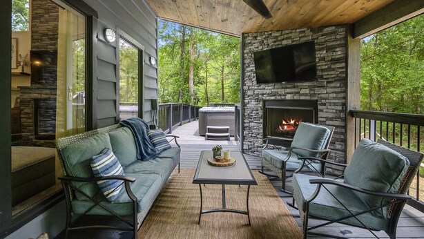 A covered deck with a stone fireplace, outdoor seating, and a TV mounted on the wall.
