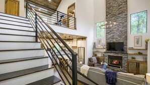 A spacious living area with a fireplace, a staircase, and a kitchen in the background.