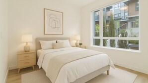 Un dormitorio con un ventanal grande, una cama con ropa de cama blanca, dos mesitas de noche con lámparas y una obra de arte enmarcada en la pared.