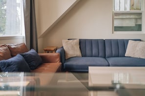 A modern living room with a blue sofa, a brown leather chair, and a glass coffee table.