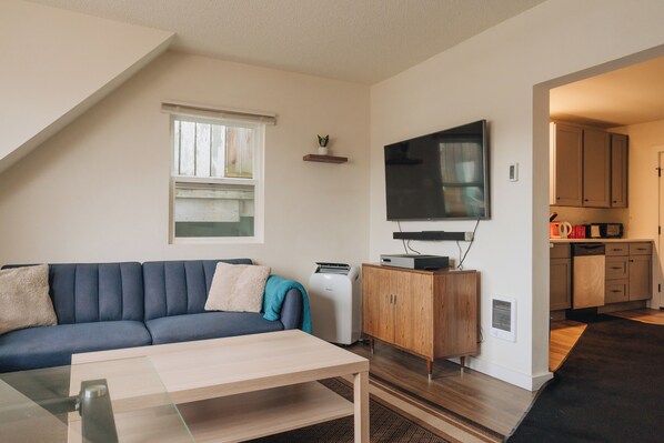A living room with a sofa, a coffee table, a flat-screen TV, a small cabinet, and a window.