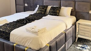 Ein modernes Schlafzimmer mit einem gesteppten Kopfteil, einem großen Bett mit weißen Leinentüchern, einem flauschigen Teppich und einem Nachttisch mit Lampe.