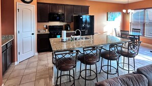 A modern kitchen with dark cabinets, a central island with bar stools, and a dining area with chairs.