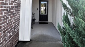 A building entrance with a brick wall, a white door, and a small porch area.