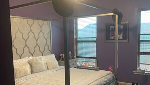 A four-poster bed with a ceiling fan, a window with blinds, and a framed picture on the wall.