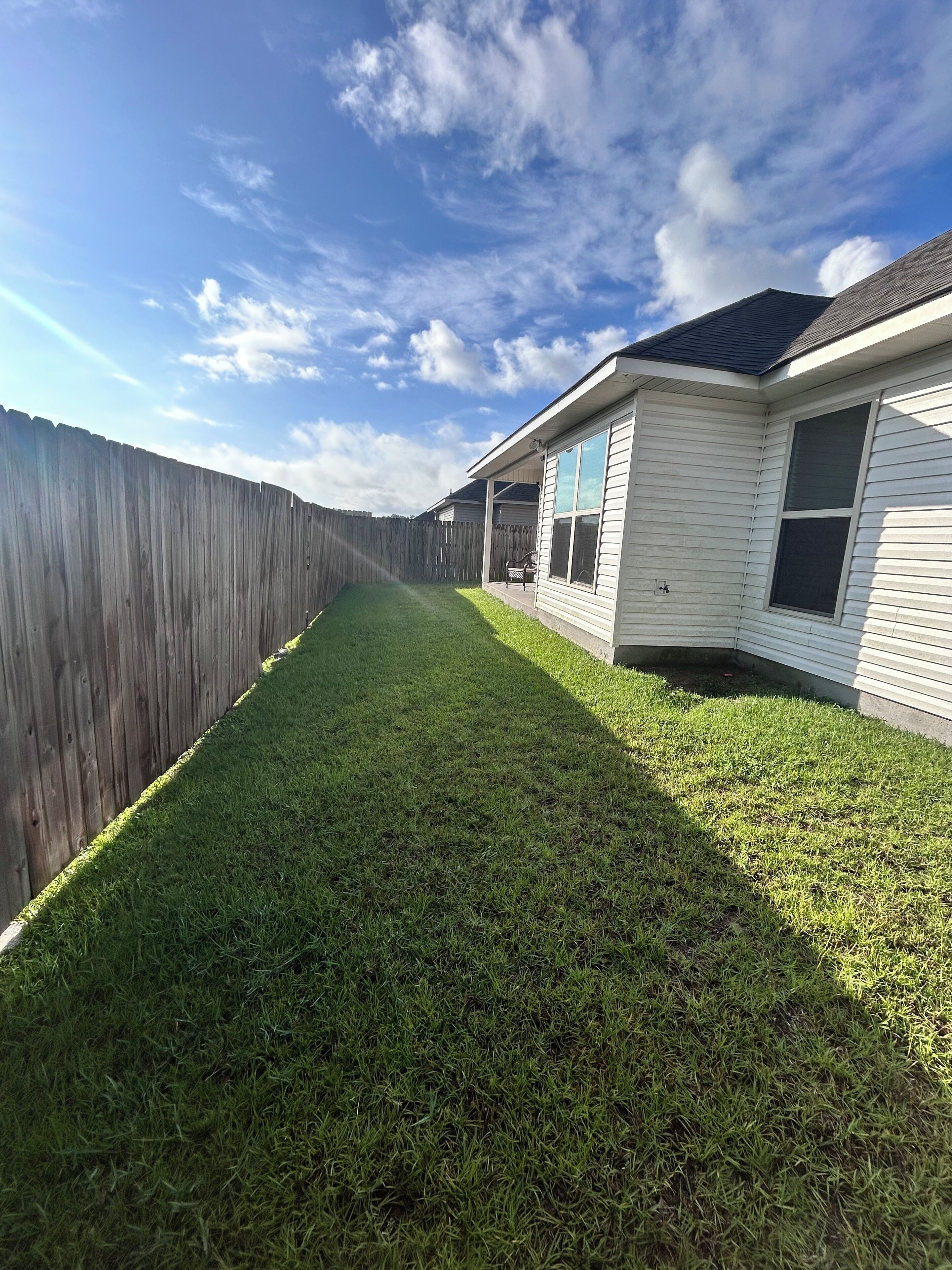 A residential backyard with a wooden fence, a lawn, and a house with a covered patio area.