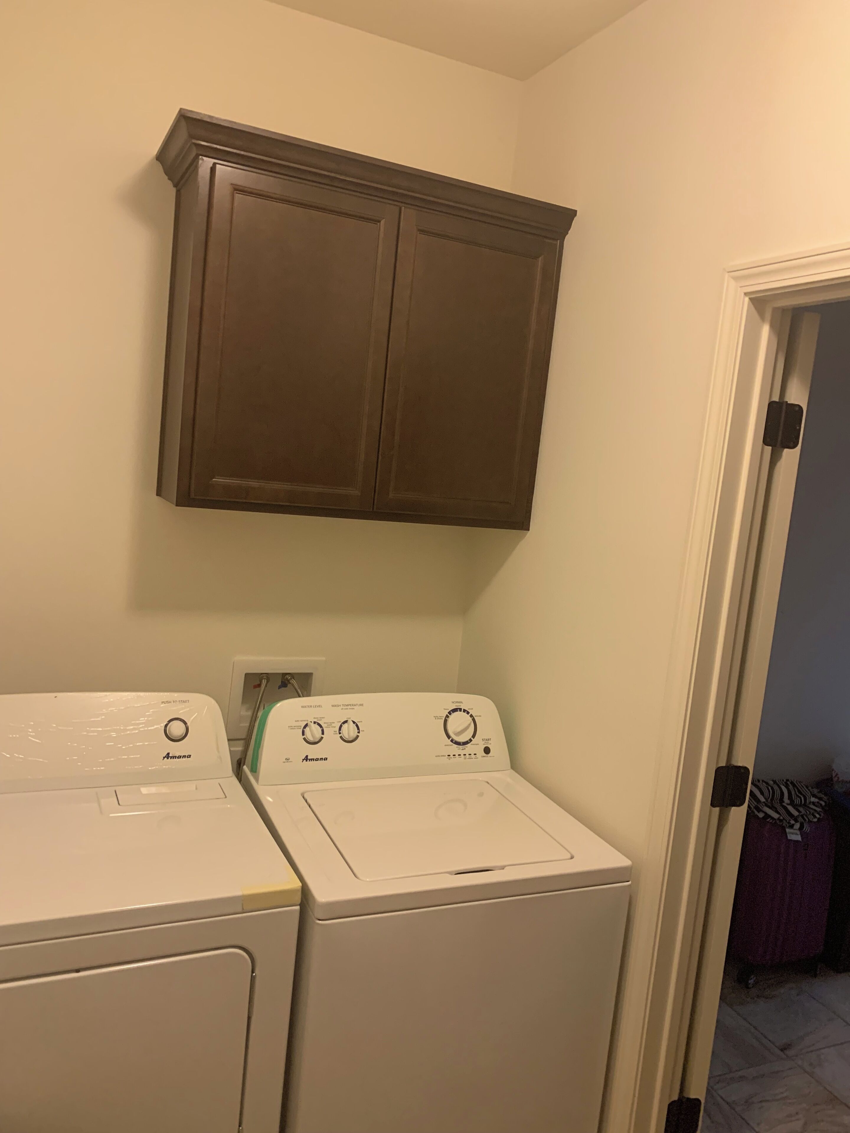 A laundry room with two white front-loading washing machines and a wooden cabinet above them.