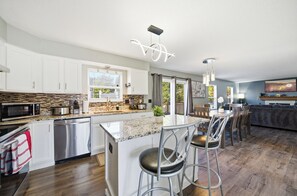 A modern kitchen with white cabinets, stainless steel appliances, and a central island with bar stools. - Spacious 4-BR Retreat w/ Game Room + BBQ Patio (Hilliard)