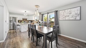 Eine moderne Küche mit weißen Schränken, einem Edelstahlkühlschrank und einem Essbereich mit einem Holztisch und Stühlen.