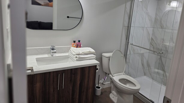 Un baño moderno con un lavabo blanco, tocador de madera oscura, un inodoro y una cabina de ducha de vidrio.