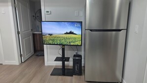 Ett kök med ett kylskåp i rostfritt stål, en platt-TV på ett stativ och en termostat på väggen.