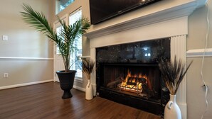 Un salon doté d’une cheminée, d’un grand téléviseur à écran plat fixé au-dessus et d’une plante en pot.