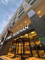 Entrada de hotel con un letrero de 'Park DeDeMan', puertas de vidrio y un mostrador de recepción.