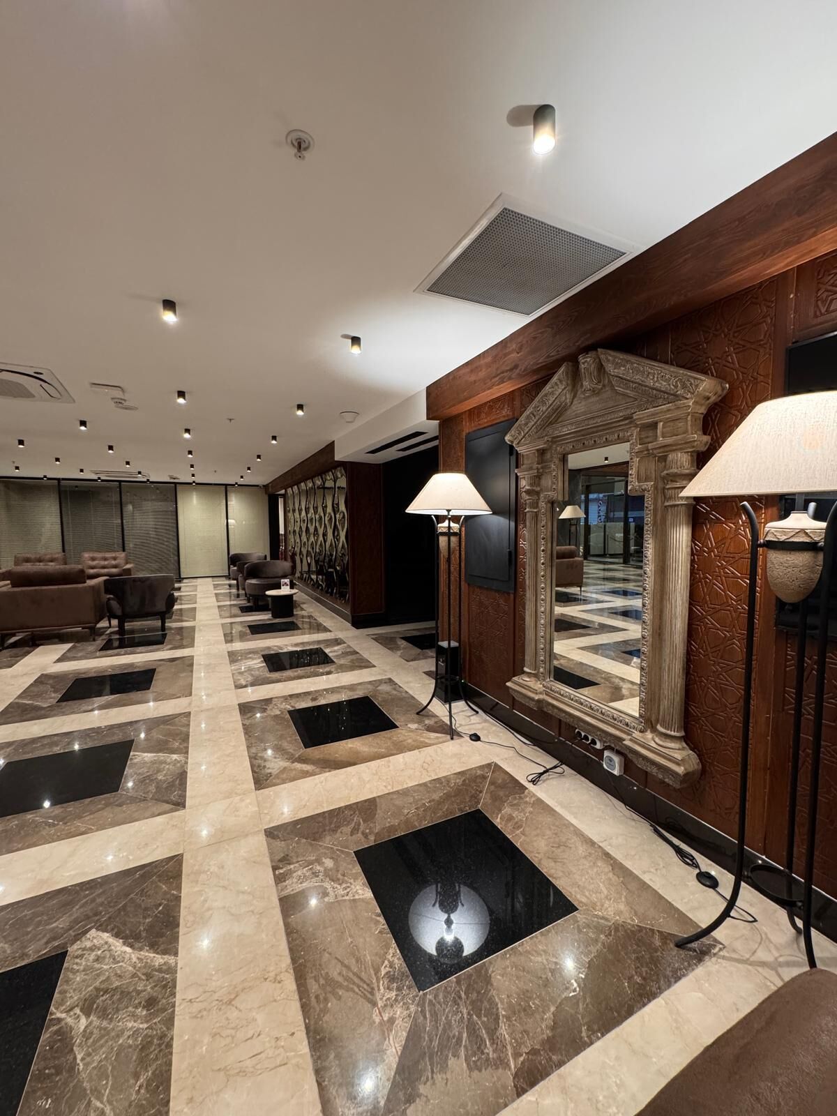 A hotel lobby with a checkered marble floor, sofas, and a large mirror with wall sconces.