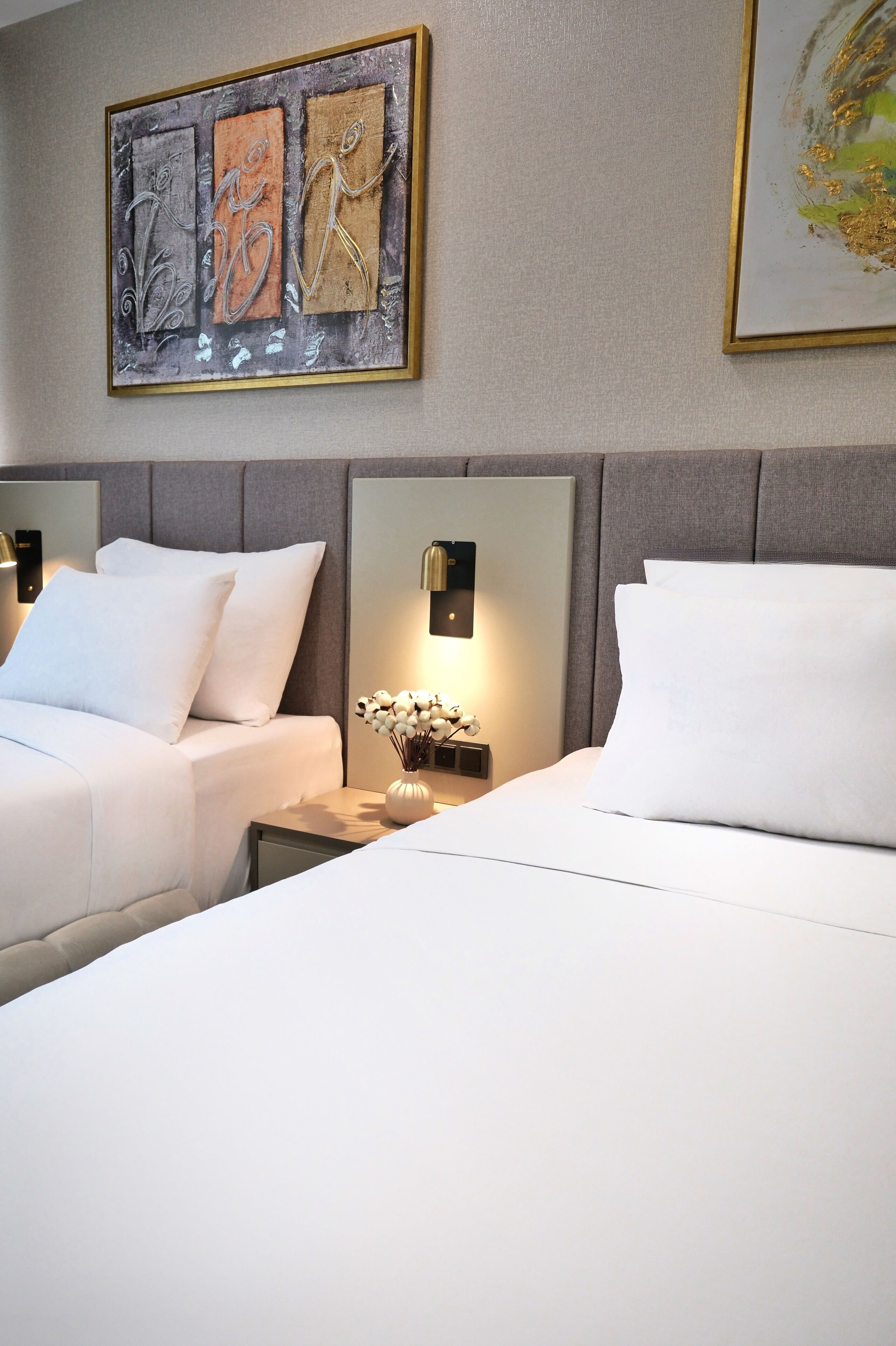 A hotel room with two beds, a nightstand with a lamp, and artwork on the wall.