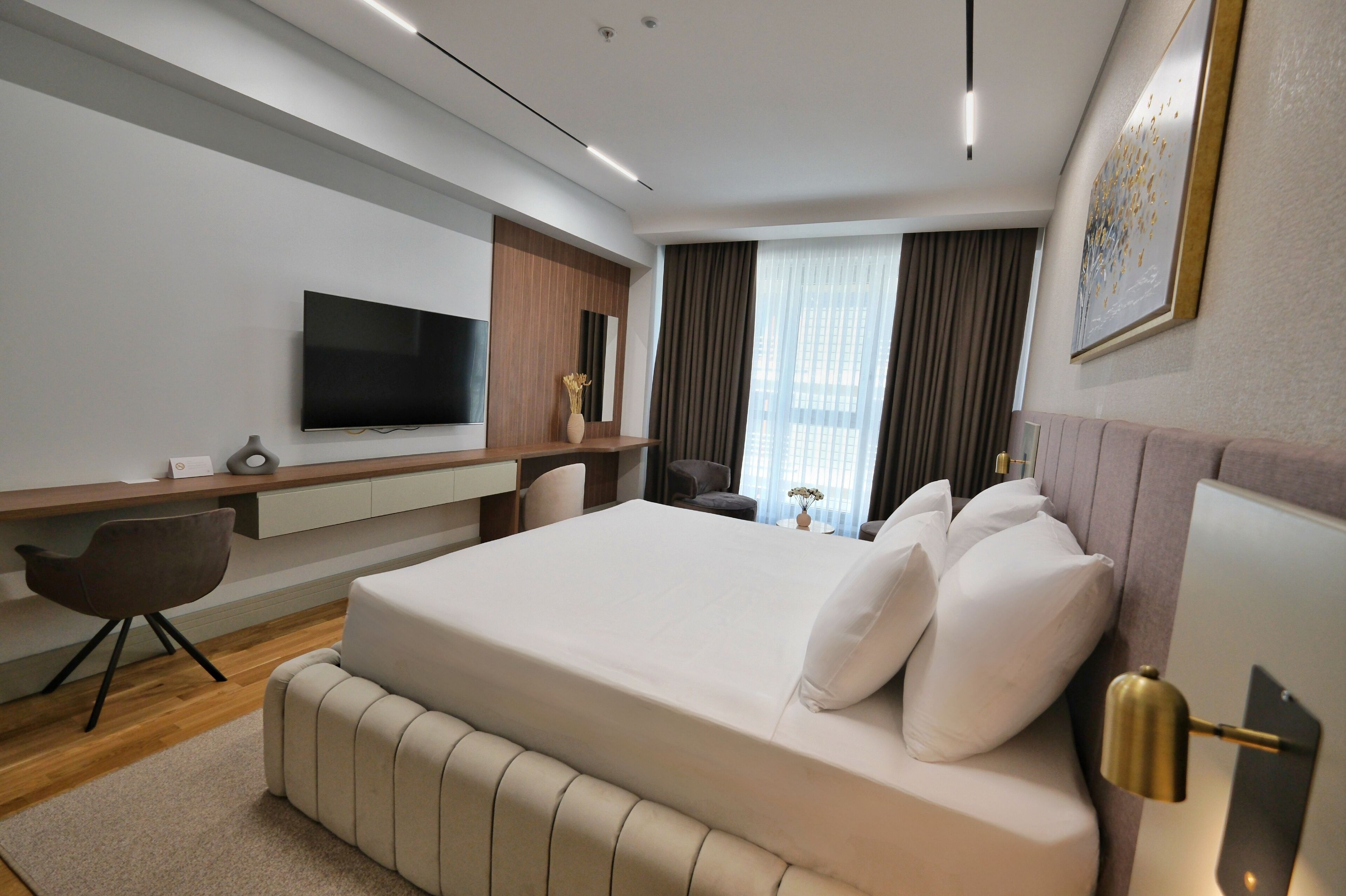 A modern hotel room with a large bed, a flat-screen TV, a desk, and a comfortable chair.