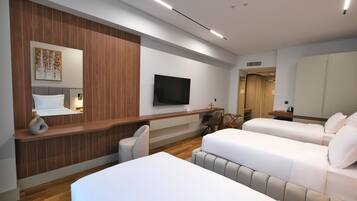 A modern hotel room with a wooden accent wall, a flat-screen TV, two beds, a desk with a chair, and a small table with a vase.