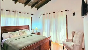 Un dormitorio con una cama de madera, una silla, un ventilador de techo y cortinas.