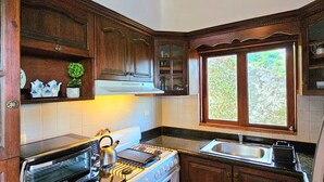 Una cocina con armarios de madera, una estufa, un tostador y una ventana con vistas al verdor.