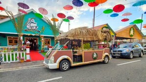 Un camión de comida con temática tropical estacionado frente a un restaurante con llamativos sombrillas de colores.