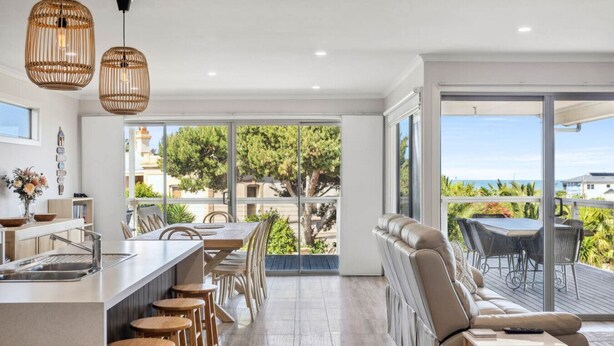 A modern kitchen with a bar area, wooden stools, and a view of the outdoors. - Wave Riders in Goolwa Beach (Goolwa Beach)