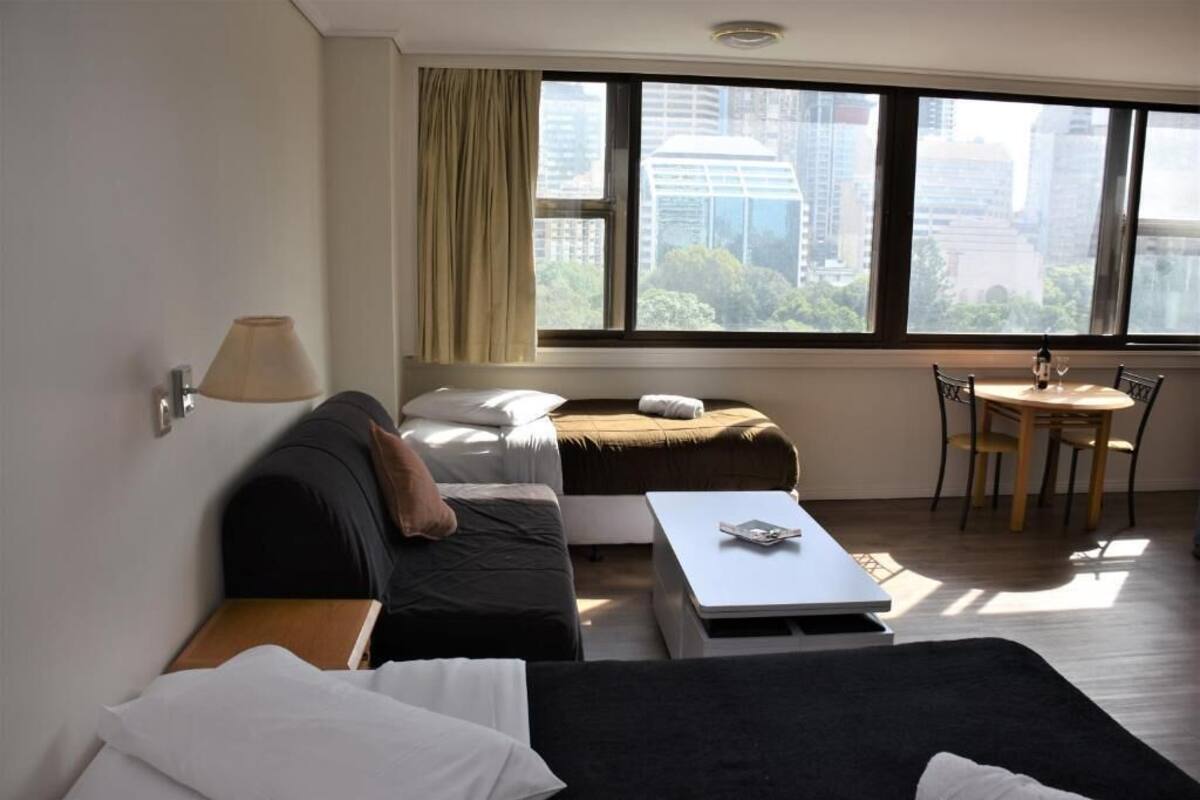 A hotel room with a bed, a sofa, a small table, and a window with a city view.