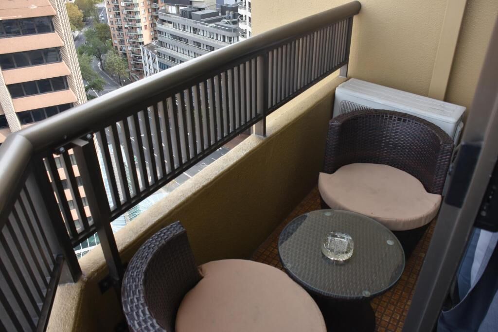 A balcony with wicker furniture and a small table, overlooking a cityscape.
