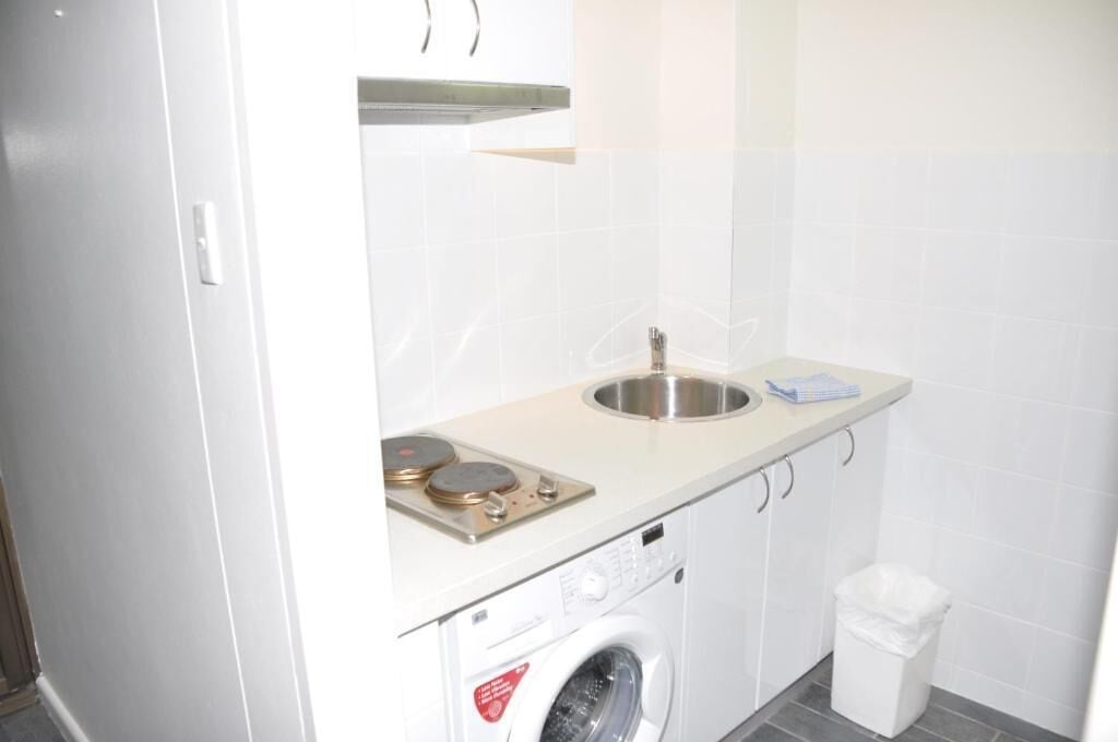 Une cuisine compacte équipée d’un lave-linge encastré, d’un évier et d’un petit plan de travail.