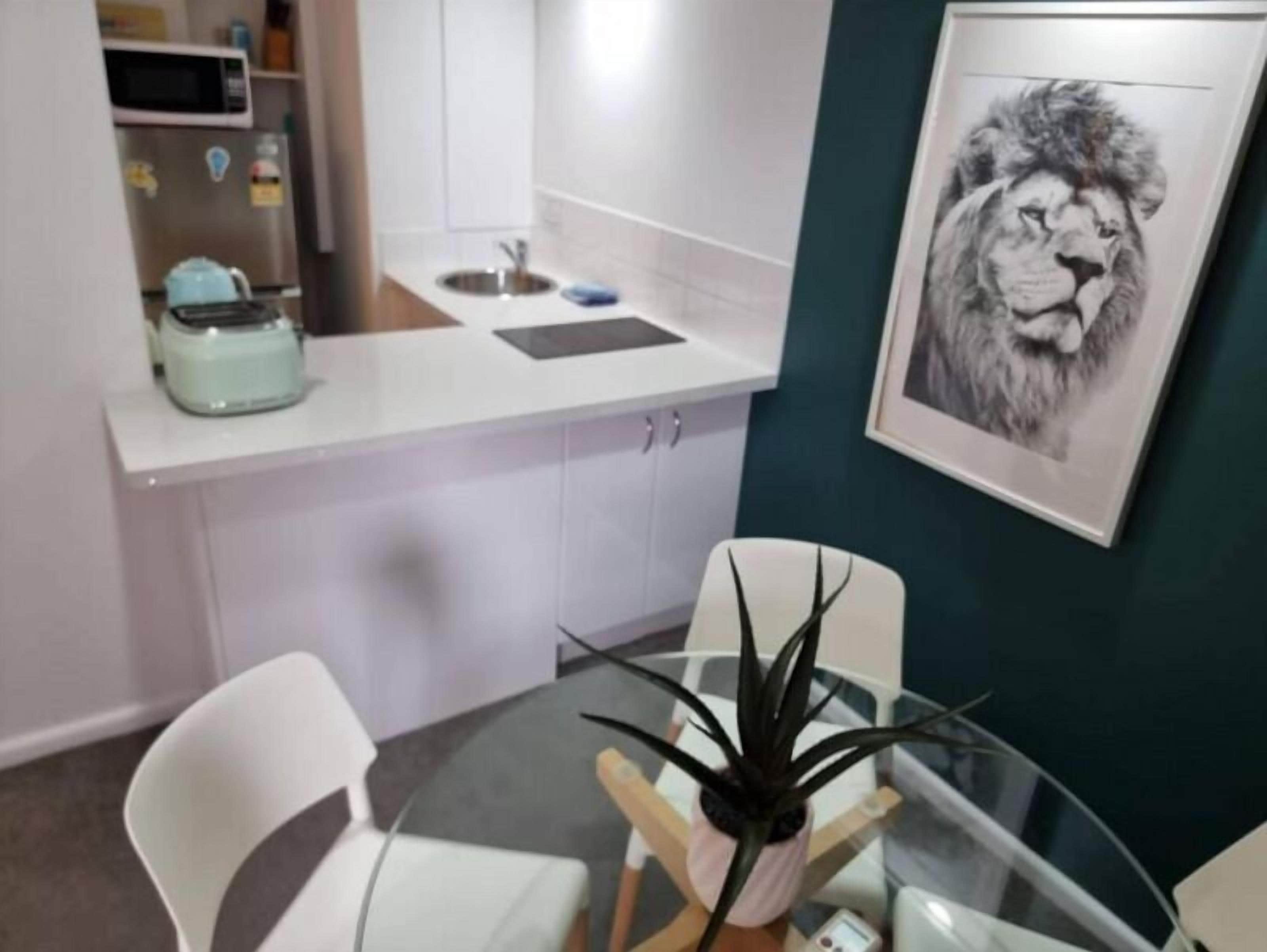 A modern kitchen with white cabinets, a stainless steel sink, and a microwave. There is a framed picture of a lion on the wall.