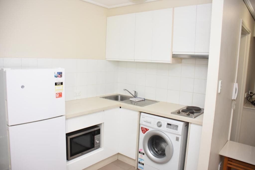 A compact kitchen with a refrigerator, microwave, washing machine, and a sink.