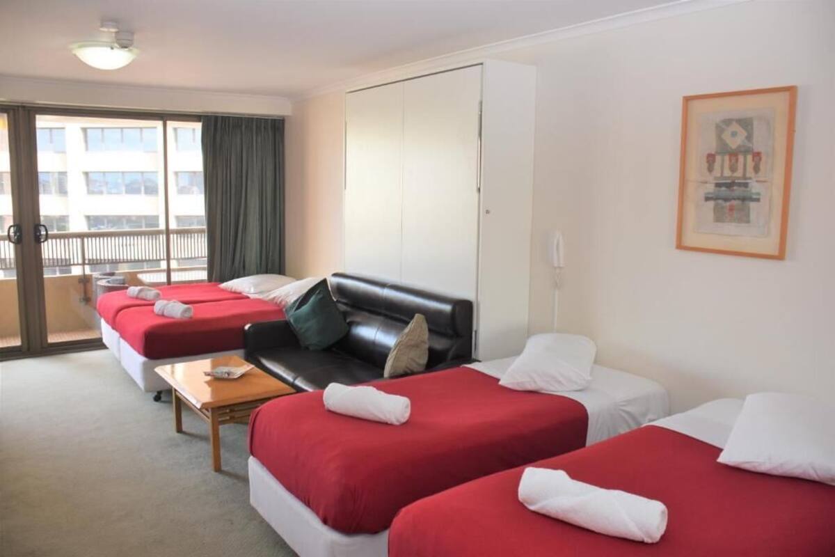 A hotel room with two beds, a sofa, a small table, and a balcony with curtains.