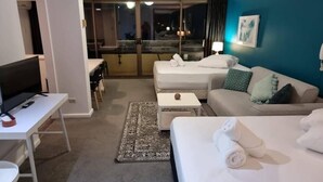 Habitación de hotel con cama, sofá, escritorio con computadora y vista al balcón exterior.