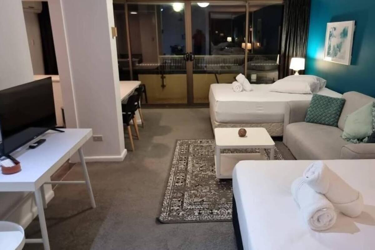 A hotel room with a bed, a sofa, a desk with a computer, and a view of the outside balcony.