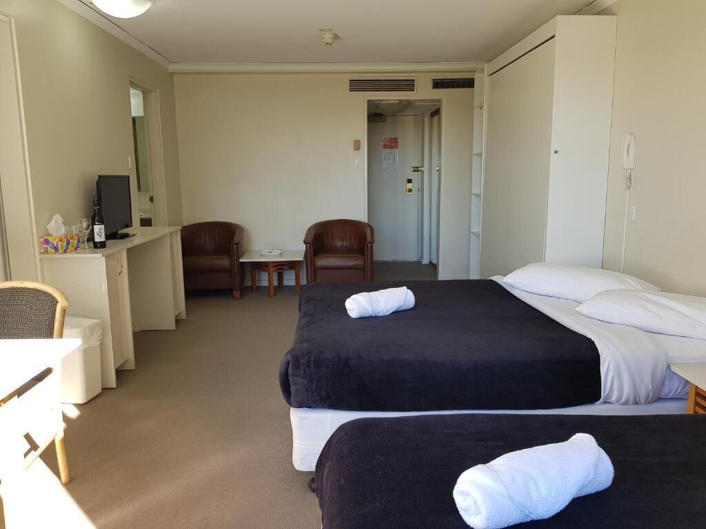 A hotel room with two beds, a desk with a computer, a chair, and a small table.