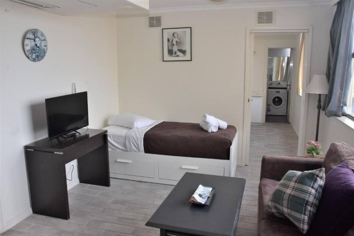A compact hotel room with a bed, a desk with a TV, a small table, and a couch.