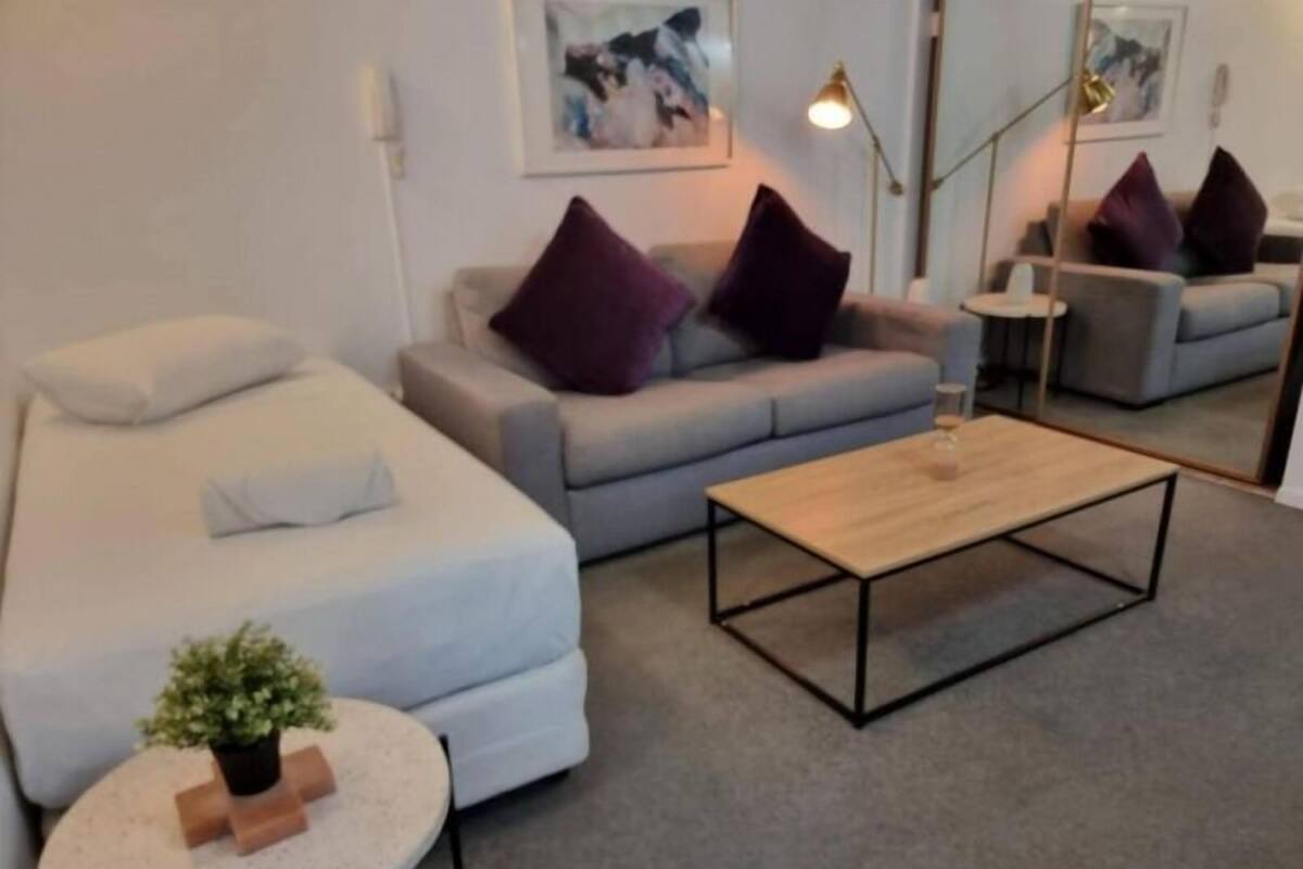 A modern living room with a grey sofa, a wooden coffee table, and a small round table with a plant.