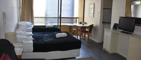 A hotel room with two beds, a desk, a television, and a balcony.