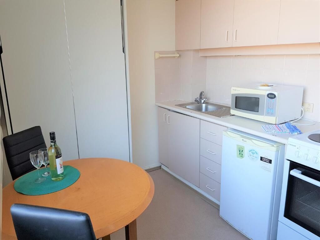 Ett kompakt kök med diskho, mikrovågsugn, kylskåp och ett matbord med stolar.