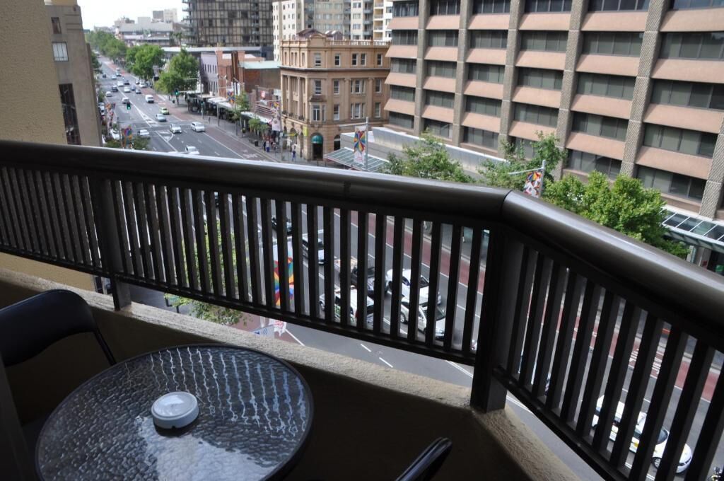 Un balcón con vistas a una calle de la ciudad, una mesa con una taza y una silla.