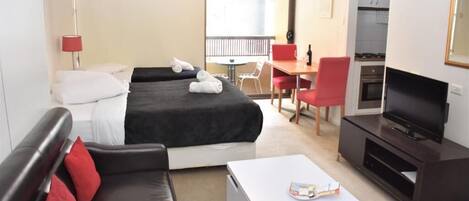 Une chambre d’hôtel comprenant un lit, un canapé, une télévision, une table à manger et un coin cuisine.