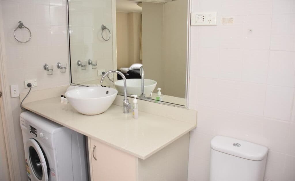 Un baño con lavabo, espejo y lavadora.