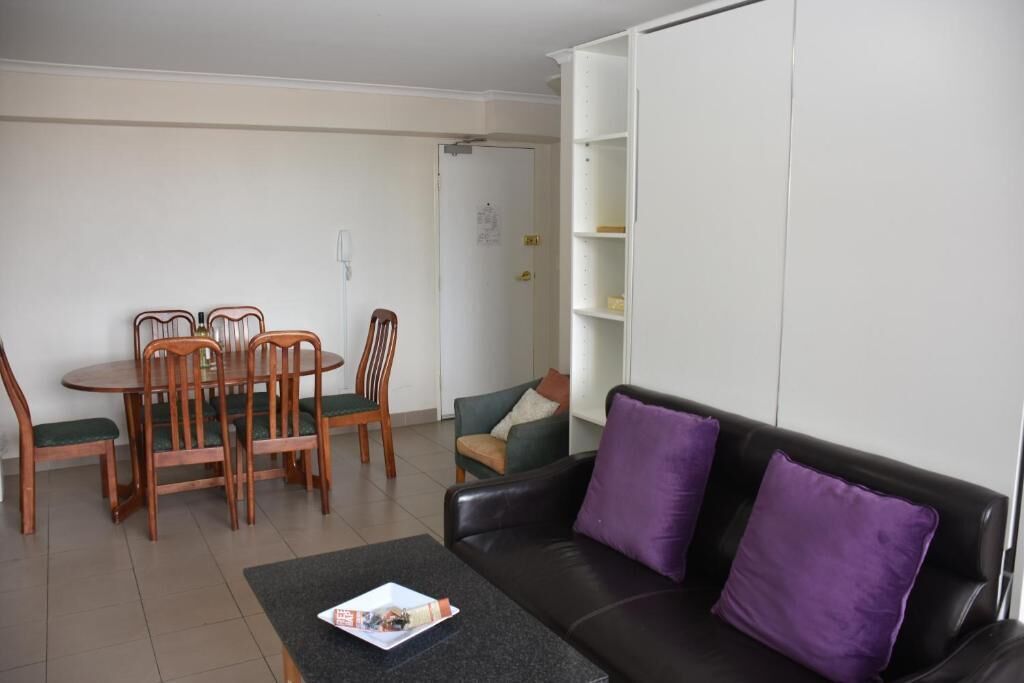 A living room with a black leather sofa, green cushioned chairs, a dining table, and a white shelving unit.
