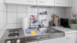 A modern kitchen with white cabinets, a stainless steel sink, and a stove. - Crans-Montana - Studio 2 pp - Centre/Rue du Prado (Lens)